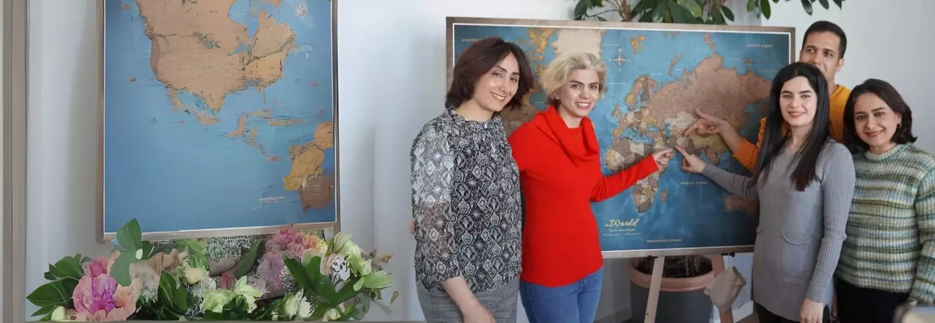 Auf dem Bild ist links eine Gruppe von 5 Personen zusehen. Drei Personen aus dieser Gruppe zeigen mit ihrem Finger auf eine Weltkarte.